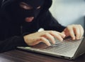 Close up of a ill-intentioned hacker in black balaclava entering the data on a laptop. Computer hacker commits cyber crime. A Royalty Free Stock Photo