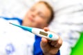 Ill young child or schoolboy, lying in bed shows blank display of electronic or digital thermometer.Blurred background Royalty Free Stock Photo