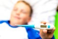 Ill young child or schoolboy, lying in bed shows blank display of electronic or digital thermometer.Blurred background Royalty Free Stock Photo