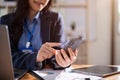 A businesswoman is checking SMS or sending messages on her smartphone while sitting at her desk Royalty Free Stock Photo