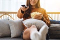 A beautiful young woman eating pop corn and searching channel with remote control to watch tv while sitting on Royalty Free Stock Photo