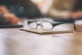 Black eyeglasses on notebook with blur businessman in office