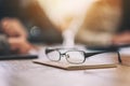 Black eyeglasses on notebook with blur businessman in office