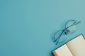 A close-up image of a book lying open with eyeglasses resting next to it on a light blue surface. Generative AI Royalty Free Stock Photo