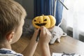 Close up image of boy holds orange round pumpkin and draws smiling face on it.