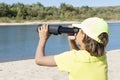 Close up image of boy sits on the river bank, holds a telescope in his hands and looks through it into the distance