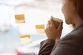 Close-up image of a businesswoman is looking at sticky notes on a wall while sipping coffee Royalty Free Stock Photo