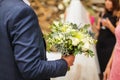 Close up image of caucasian groom in suit holds wedding bouquet in arm in selective focus