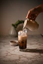 Close-up image, Female barista`s hand pouring a fresh milk into a glass of iced coffee Royalty Free Stock Photo