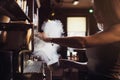 Close-up image of female barista using coffee-making machine to steam milk in cafe