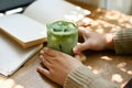 Close-up image of a female holding a glass of iced matcha green tea at a table