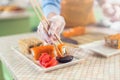 Close-up image of female hand in glove holding a sushi roll in chopsticks dipping it in soy sauce in kitchen Royalty Free Stock Photo