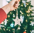 Close up image of female hand hanging Christmas wooden star decoration on spruce tree. Unfocused green branches bokeh with new Royalty Free Stock Photo