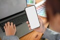 Close-up image, Female using a smartphone while typing on laptop keyboard in her workspace Royalty Free Stock Photo