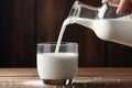 Creamy milk being poured into a glass from a bottle on warm brown background Royalty Free Stock Photo