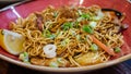 Oriental stir fried noodles served in red bowl close up