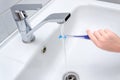 Close up image of a hand holding a blue toothbrush. water being poured on toothpaste on top in bathroom sink Royalty Free Stock Photo