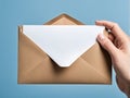 Hand holding brown envelope with white paper on blue background Royalty Free Stock Photo