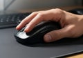 A close-up image of a hand resting on a black computer mouse, positioned on a dark Royalty Free Stock Photo