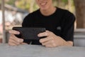 Close-up image of a happy young Asian man playing a mobile game while sitting at a table outdoor Royalty Free Stock Photo