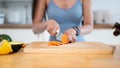 A fit woman in gym clothes is slicing carrots on a chopping board, preparing her healthy breakfast