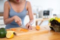 A fit woman in gym clothes is slicing carrots on a chopping board, preparing her healthy breakfast