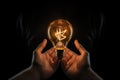 Close-up image of human hands holding incandescent light bulb, Conceptual image of a lightbulb in hand against a black background Royalty Free Stock Photo