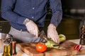 Close up image of man in casual clothers and gloves is cutting onion for salad Royalty Free Stock Photo