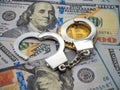 Close-up image of a pair of handcuffs on a Bitcoin coin over a pile of dollar bills