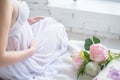 Close-up Image of pregnant woman in nice white dress touching her belly with hands and holding a bouquet of peonies. Beautiful Royalty Free Stock Photo