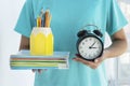 close up image of school girl holds alarm clock and school supplies in her hands on light background. Royalty Free Stock Photo