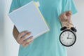close up image schoolgirl holds black alarm clock and stack of notebooks in her hands on light background Royalty Free Stock Photo