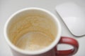 Empty red coffee mug with espresso crema residue on white desk and blurred wireless mouse minimal modern workspace close view Royalty Free Stock Photo