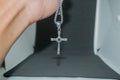 Close-up image of a man holding a silver metal christian cross necklace/pendant or silver metal crucifix necklace/pendant hanging