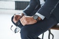 Close-up image of a stylish businessman who is sitting on the chair with branded watch on his hand and holding glasses