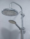 Close-up image of two shower heads in white tile bathroom. large is mounted on metal pipe and small attached to flexible hose