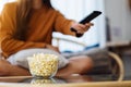 A woman eating pop corn and searching channel with remote control to watch tv while sitting on sofa at home Royalty Free Stock Photo