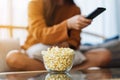 A woman eating pop corn and searching channel with remote control to watch tv while sitting on sofa at home Royalty Free Stock Photo