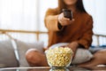 A woman eating pop corn and searching channel with remote control to watch tv while sitting on sofa at home Royalty Free Stock Photo