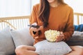 A woman eating pop corn and searching channel with remote control to watch tv while sitting on sofa at home Royalty Free Stock Photo