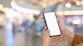 Close-up image of woman hand while using/holding a white blank screen smartphone over the blurred supermarket background. Royalty Free Stock Photo