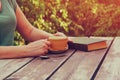 Close up image of woman reading book outdoors, next to wooden table and coffe cup at afternoon. filtered image. filtered image. Royalty Free Stock Photo