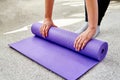 Close up image of woman rolling purple fitness or yoga mat after sport practice, pilates or working out at home