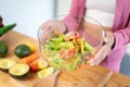 Close-up image of a woman in sportswear holding a bowl of healthy fresh salad over the kitchen table Royalty Free Stock Photo