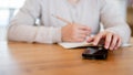 A close-up image of a woman using her phone and writing in a book at a wooden table in a cosy room Royalty Free Stock Photo