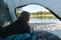 Close up image of young female lies in the tent and looks at the beautiful river out from the open window.