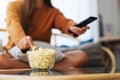 A young woman eating popcorn and searching channel with remote control to watch tv while sitting on sofa at home Royalty Free Stock Photo