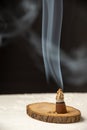 Close-up of incense lit with smoke, on wooden base, on white table, black background, vertical, Royalty Free Stock Photo