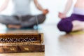 Close-up of incense stick, behind couple doing yoga.