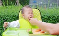 Close-up infant baby boy sitting on kid chair eating with something stuck in his mouth and mother help to keep out Royalty Free Stock Photo